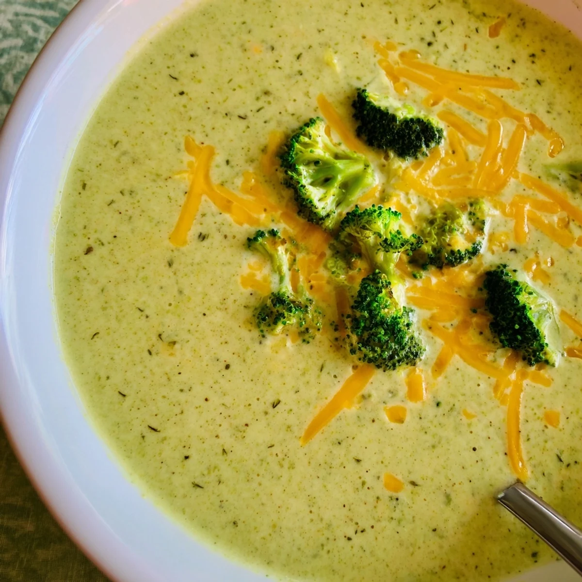 Steaming bowl of homemade broccoli cheddar soup, garnished with extra cheese and fresh broccoli florets for a comforting meal.  