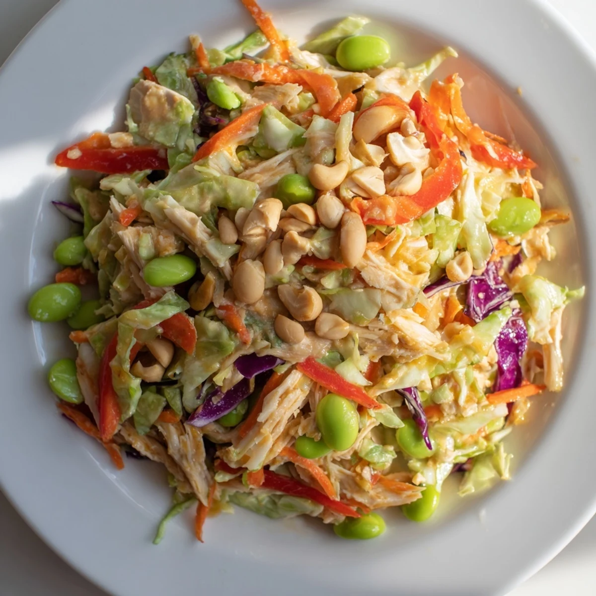 Freshly tossed Edamame Crunch Chicken Salad in a large bowl, showcasing vibrant red cabbage, shredded carrots, and tender chicken tossed with sesame seeds and edamame.