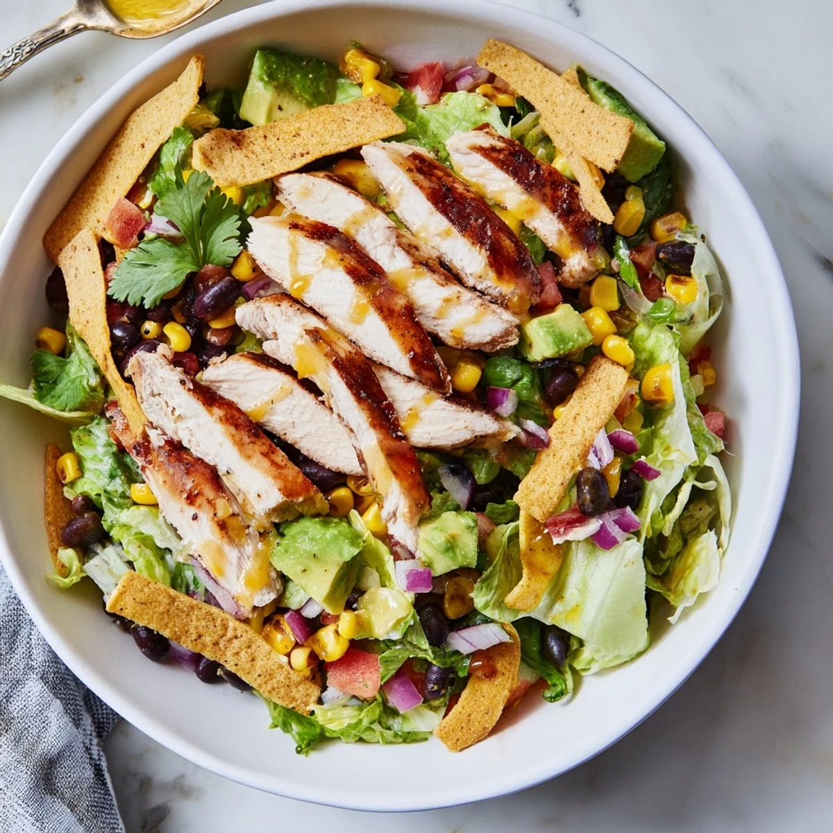Grilled Honey Lime Chicken Taco Salad with chopped romaine, corn, black beans, avocado, and shredded cheese, topped with crispy tortilla strips.  