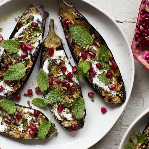 Steaming hot roasted eggplant with pomegranate bursts, creamy yogurt sauce, and fresh herbs.