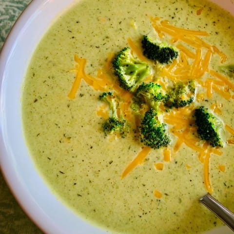 Steaming bowl of homemade broccoli cheddar soup, garnished with extra cheese and fresh broccoli florets for a comforting meal.  