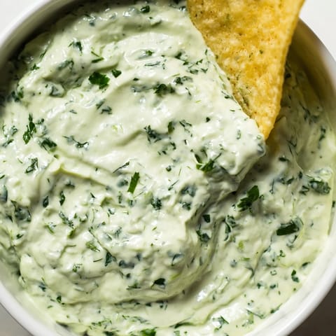 A creamy bowl of homemade Green Goddess Salad Dip garnished with fresh herbs, ready for dipping crispy tortilla chips.