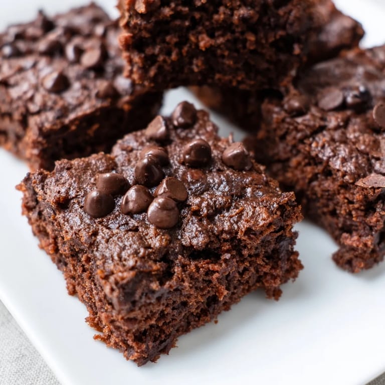 Square-cut Greek yogurt brownies, slightly cracked on top, promising a rich, chocolatey, high-protein dessert.