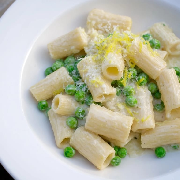 Warm bowl of Pea & Lemon Ricotta Pasta served with extra lemon zest and fresh herbs.