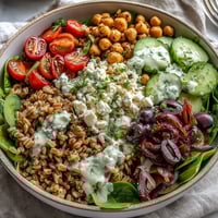 Vibrant Mediterranean farro bowl with colorful veggies, chickpeas, feta, and creamy tahini dressing in a serving dish.